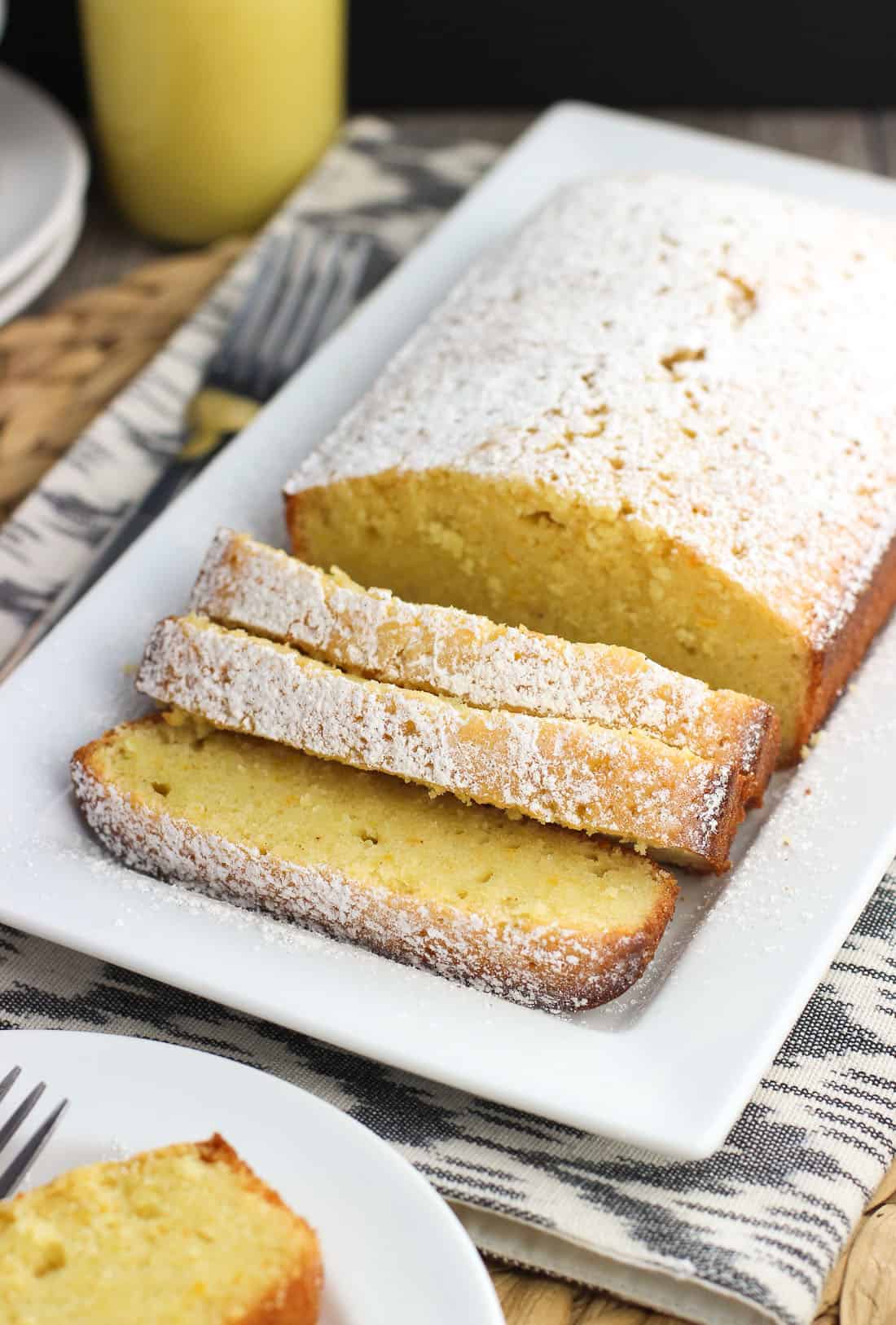 A loaf of pound cake on a tray, dusted with confectioners' sugar and cut into three slices