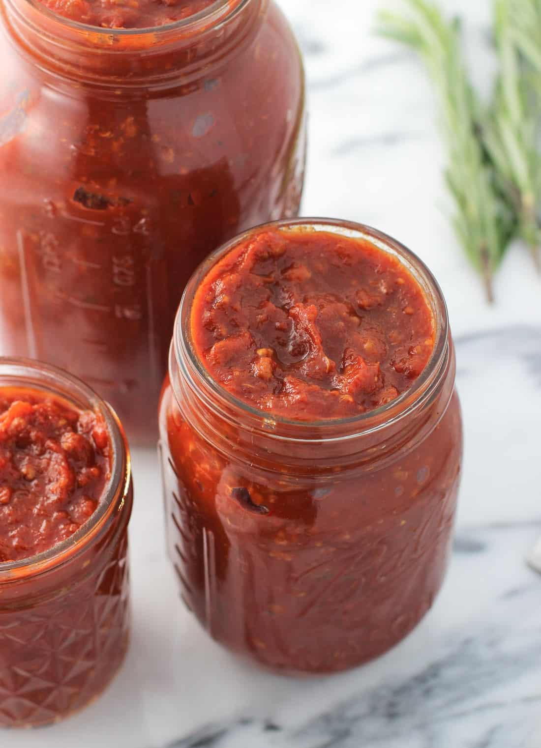 A close-up of a medium glass jar filled with sauce, surrounded by a larger and smaller jar.