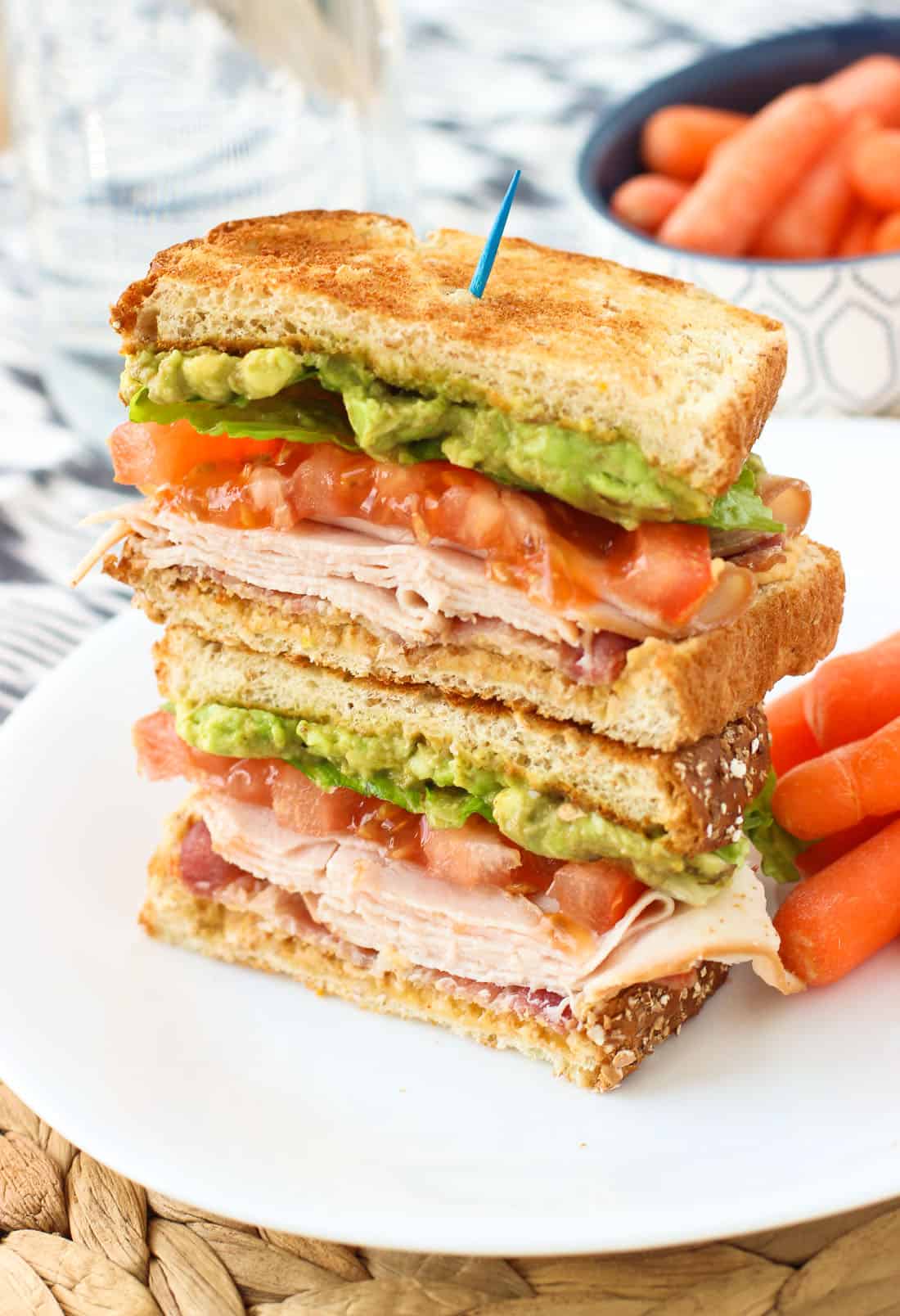 Two halves of the sandwich stacked on top of one another on a plate with baby carrots.