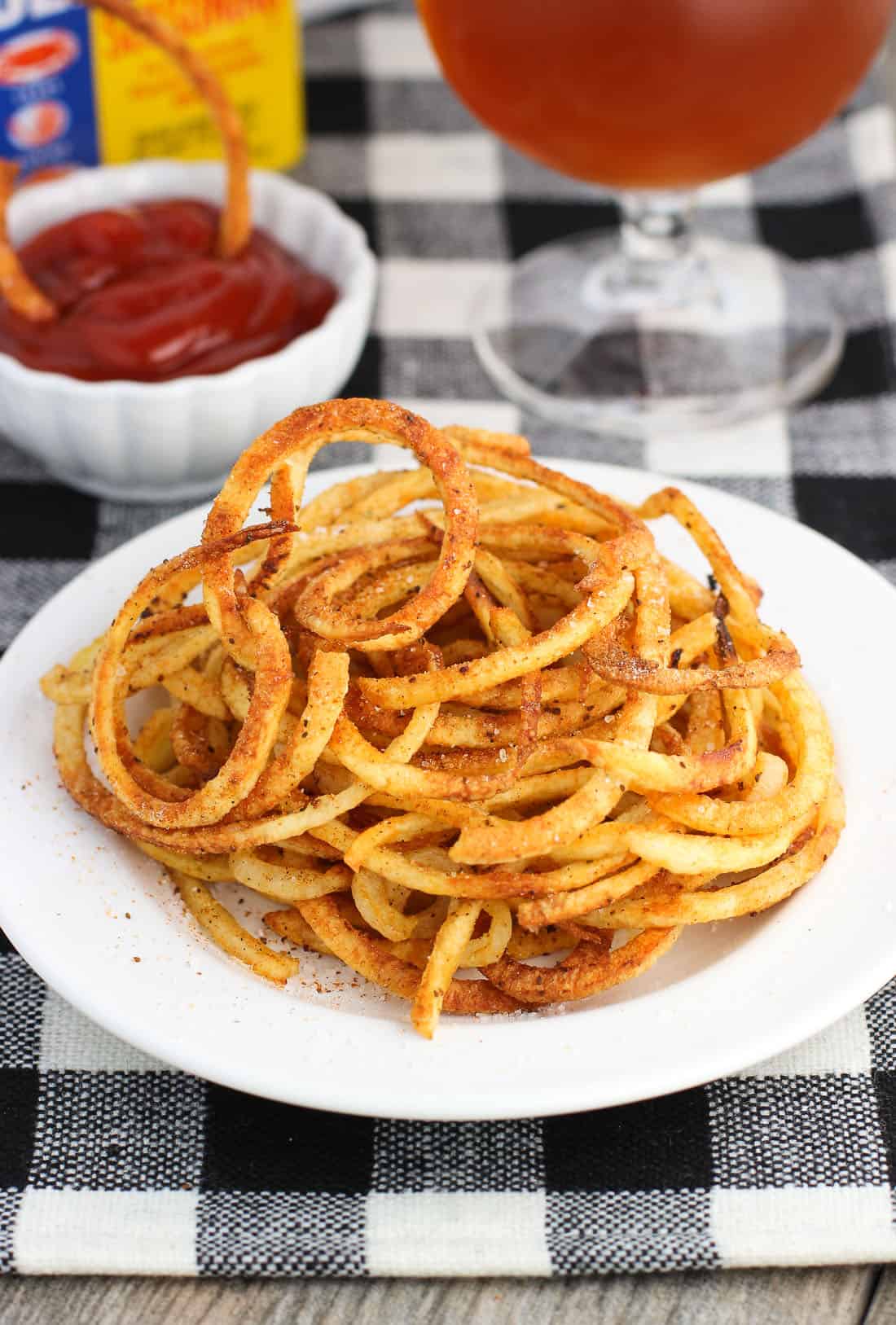 Fries on a plate with a small bowl of ketchup in the background.