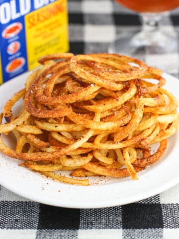 A pile of fries on a plate with a container of Old Bay seasoning in the background.