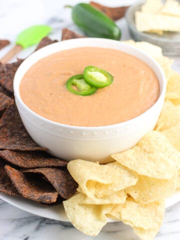 A bowl of bean dip on a plate surrounded by tortilla chips.