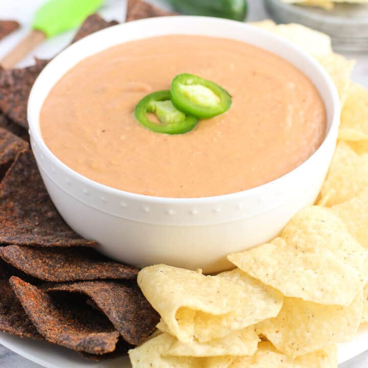 A bowl of bean dip on a plate surrounded by tortilla chips.