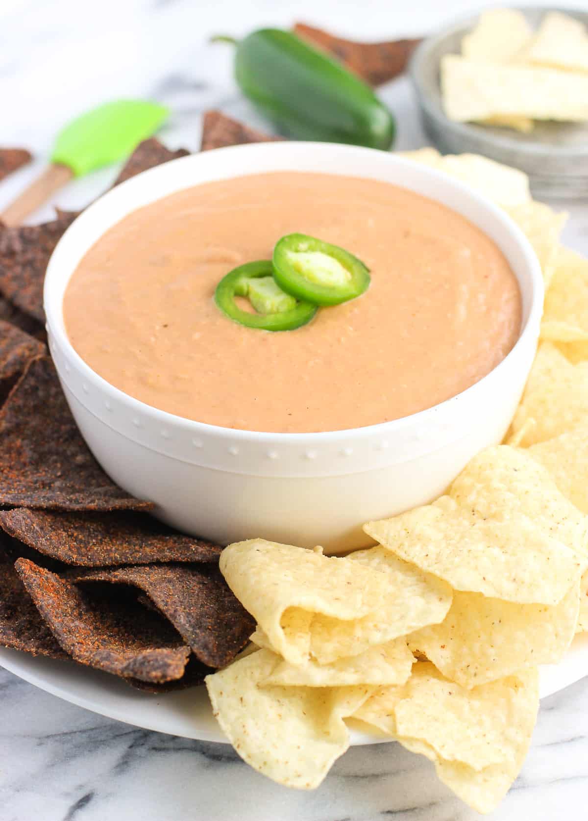 A bowl of bean dip on a plate surrounded by tortilla chips.