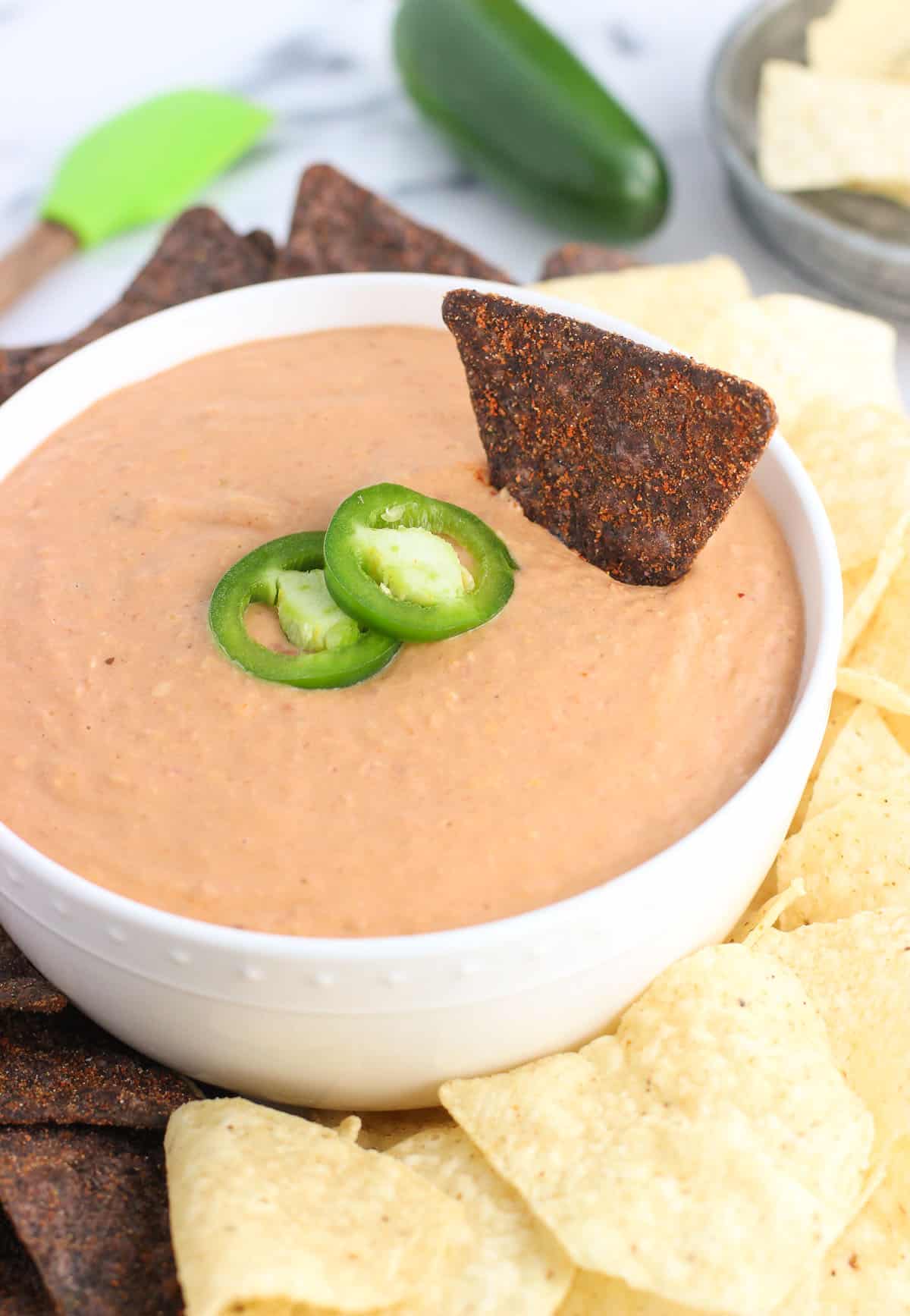 A tortilla chip dunked into the bowl of bean dip.