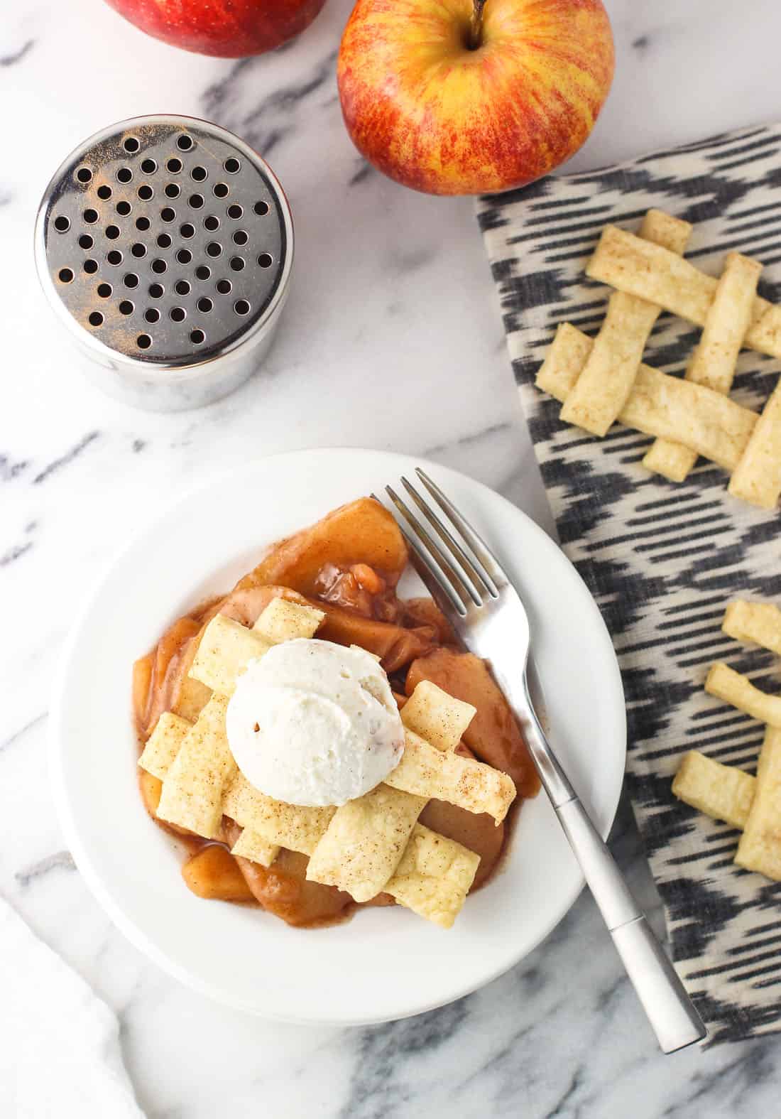 A serving of ice cream-topped slow cooker apple pie on a plate with a fork.