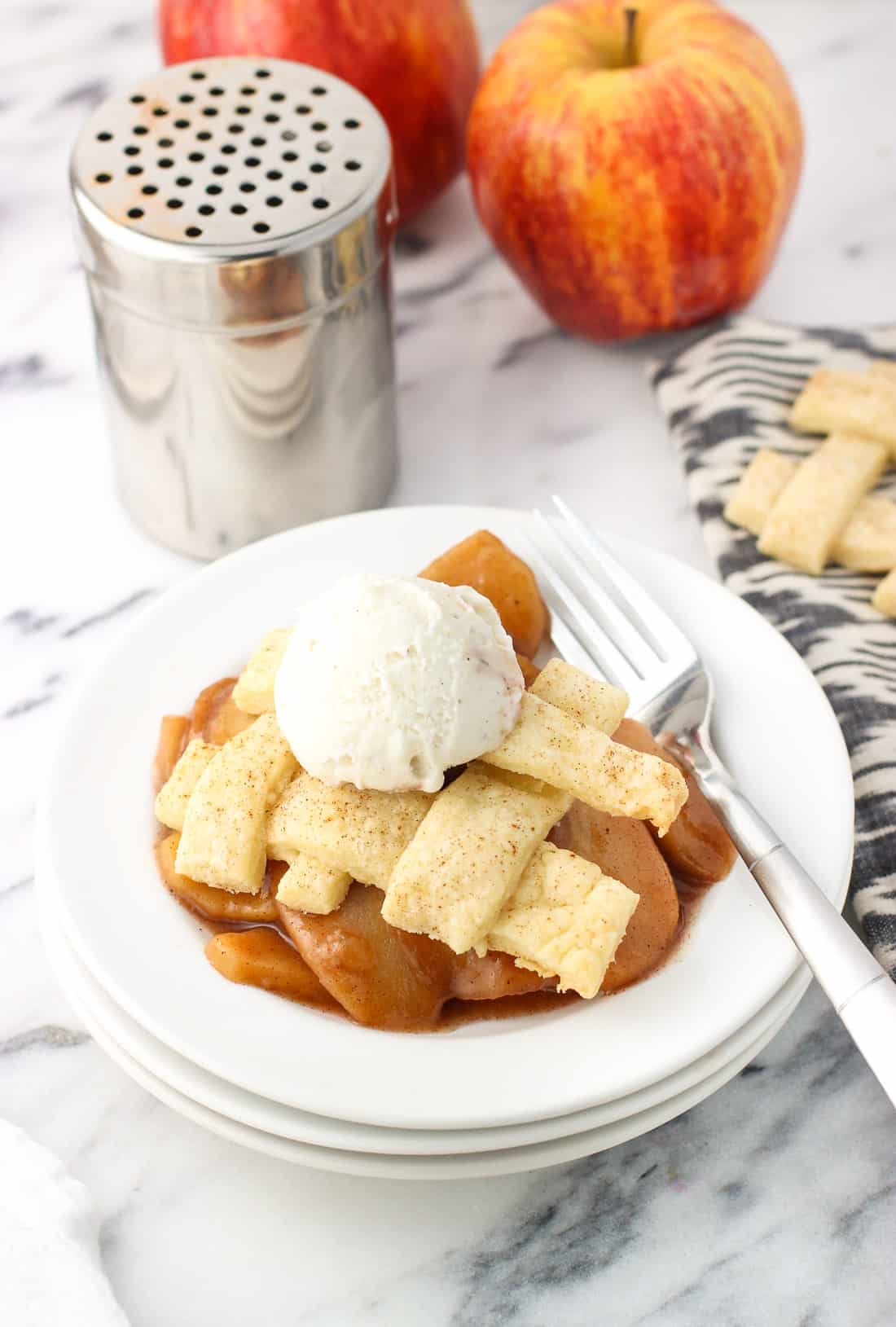 A slow cooker apple pie serving on a dessert plate with a fork and a small scoop of vanilla ice cream.