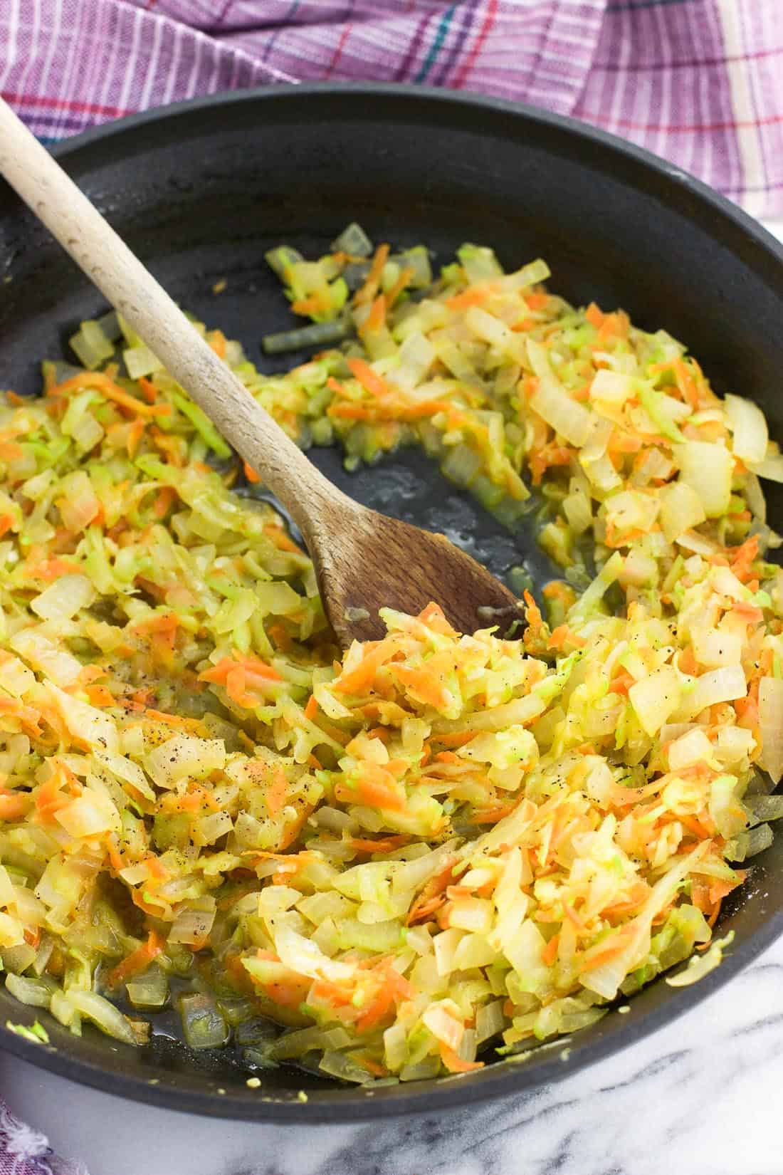 Shredded sauteed vegetables in a pan with a wooden spoon.