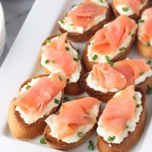 Crostini topped with burrata and a slice of smoked salmon on a tray.