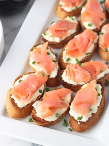 Crostini topped with burrata and a slice of smoked salmon on a tray.