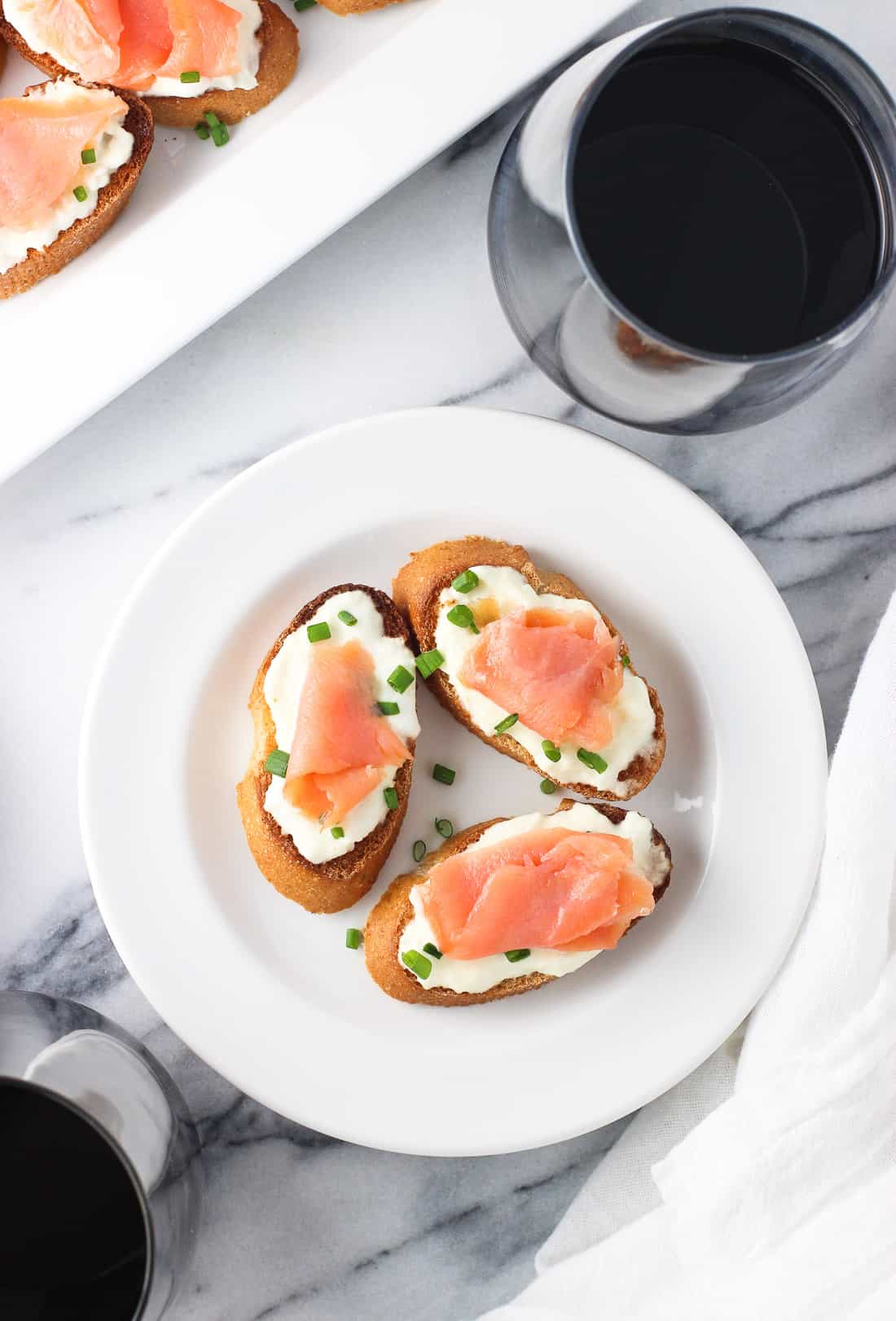 Three crostini on a plate next to a glass of wine and the crostini tray.