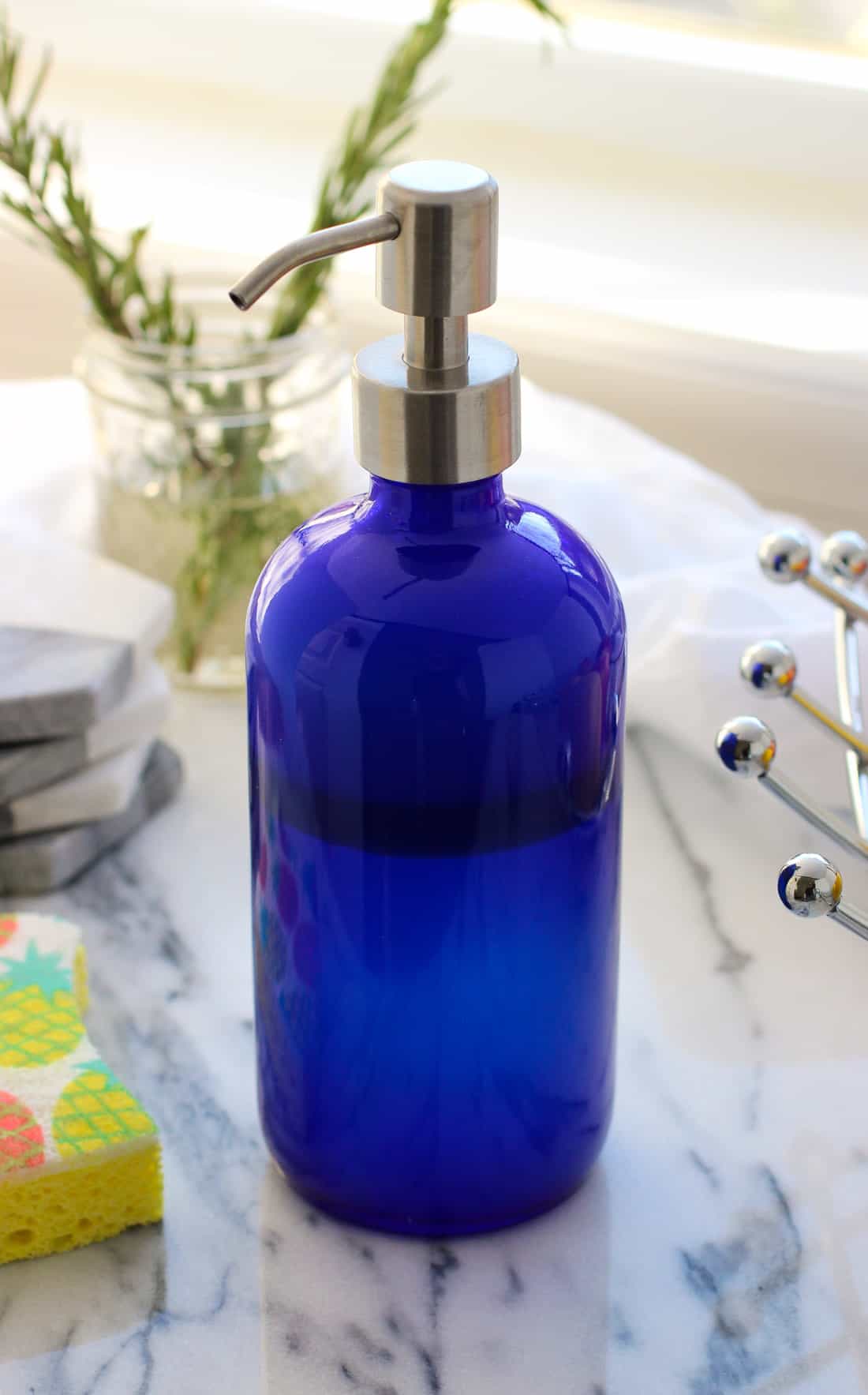 A glass soap dispenser on a table next to a sponge.