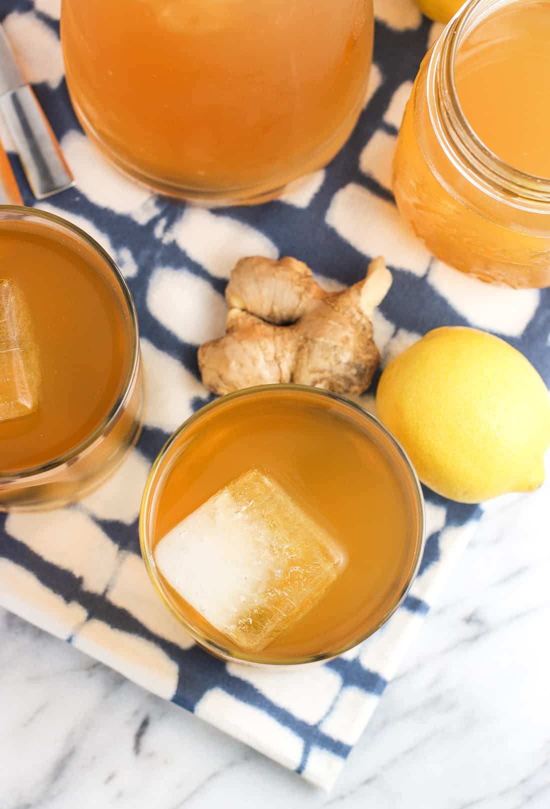 An overhead shot of two glasses of iced tea, a jar of simple syrup, a carafe of tea, piece of a ginger root and a lemon