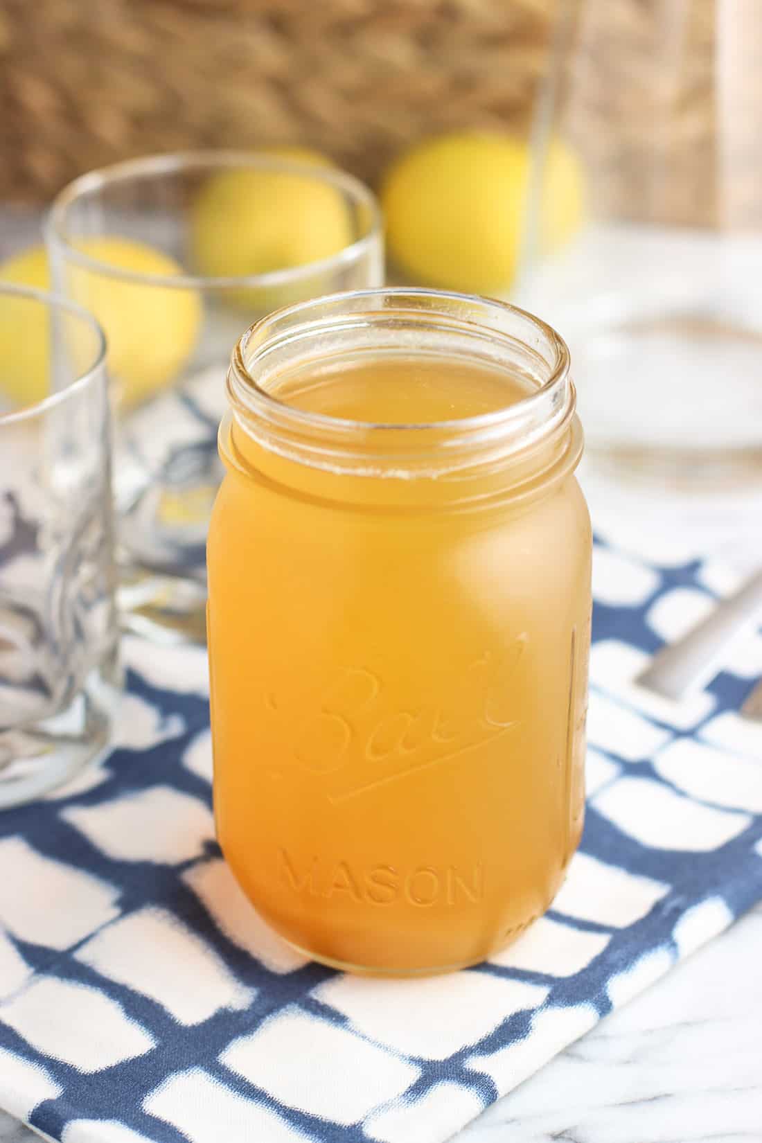 A glass jar filled with simple syrup next to empty glasses and a glass carafe for the tea