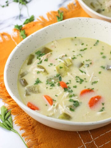 A shallow ceramic bowl of soup on a fringed linen placemat.