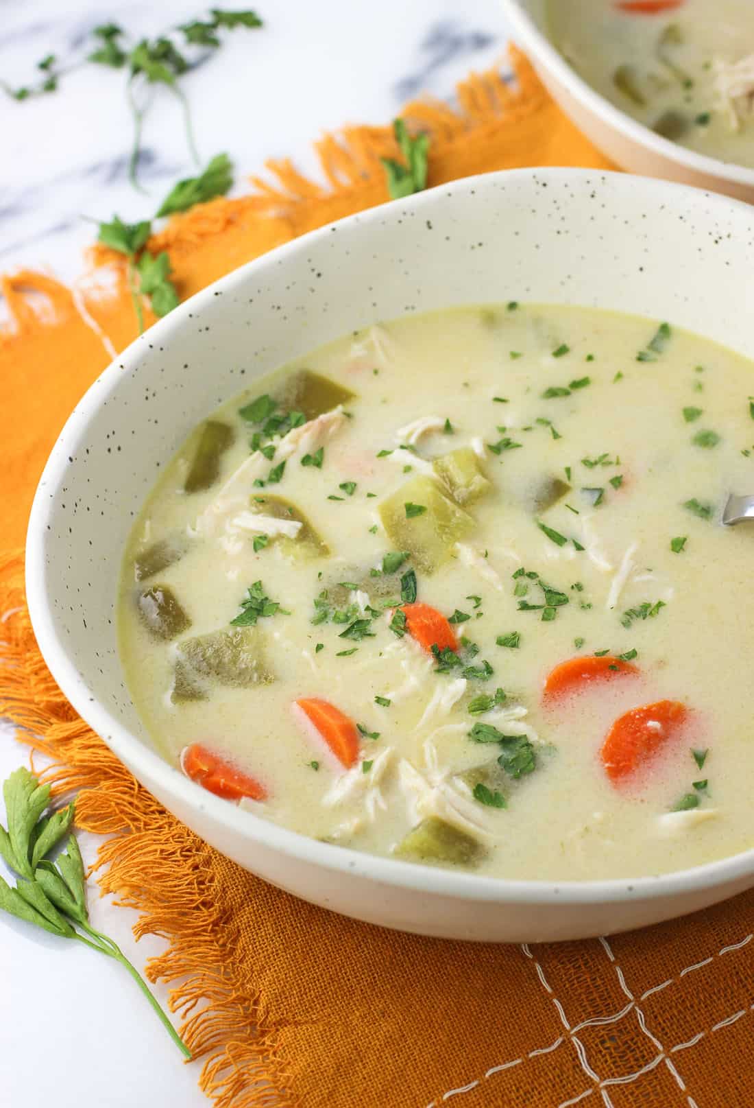 A shallow ceramic bowl of soup on a fringed linen placemat.