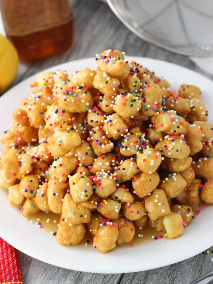 Struffoli on a plate covered in honey and rainbow nonpareils