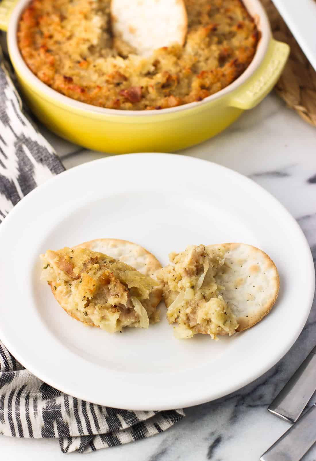 Clam dip spread onto two crackers on a small appetizer plate