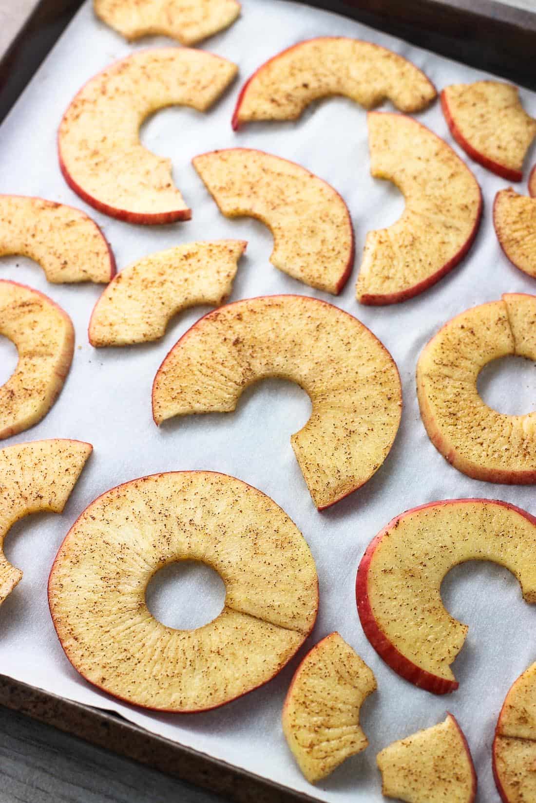 Raw spiralized apple rings sprinkled with cinnamon sugar on a parchment paper-lined rimmed metal baking sheet