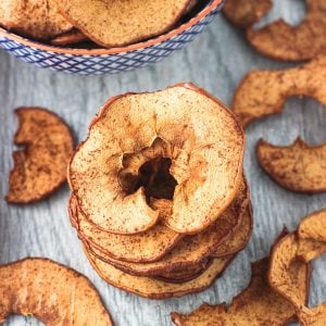 A stack of five apple chips next to scattered apple chips on a board.