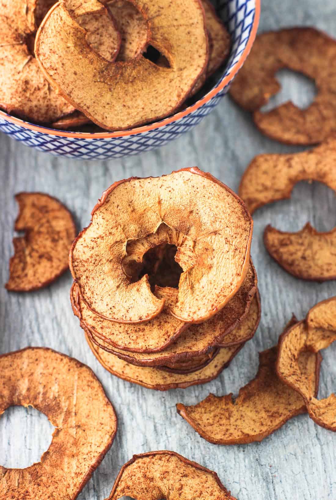 A stack of baked apple chips next to a bowl of them