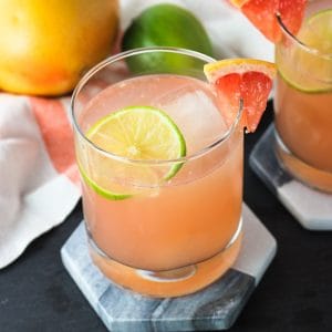 Two champagne palomas on marble coasters garnished with grapefruit wedges on the rims with lime rounds