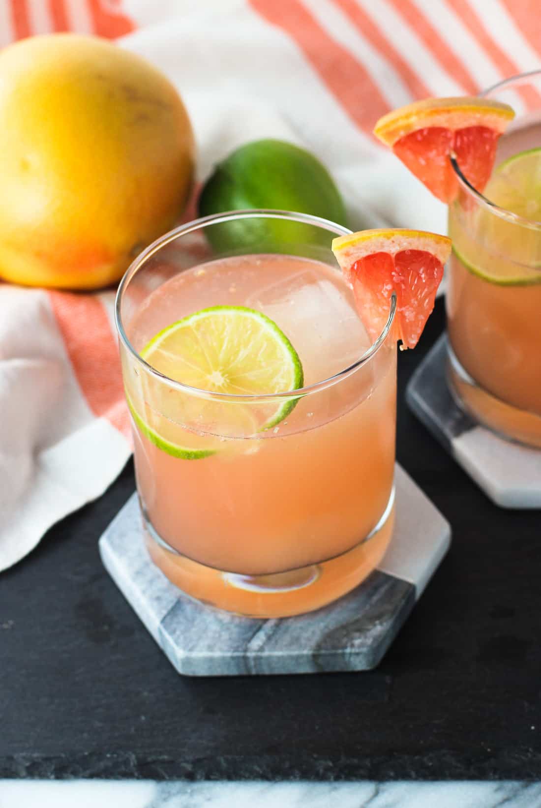 Two palomas on hexagon marble coasters beside a grapefruit and a lime