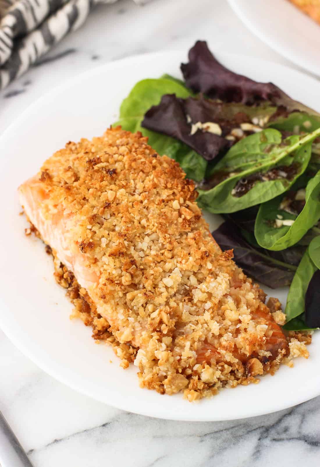 A fillet of coconut macadamia crusted salmon on a plate next to a side salad