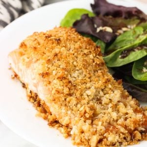 A fillet of coconut macadamia crusted salmon on a dinner plate next to a mixed greens salad