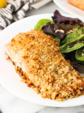 A fillet of coconut macadamia crusted salmon on a dinner plate next to a mixed greens salad