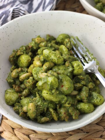 A dish of gnocchi, white beans, and sausage covered in a creamy pesto sauce with a fork