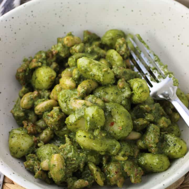 A dish of gnocchi, white beans, and sausage covered in a creamy pesto sauce with a fork