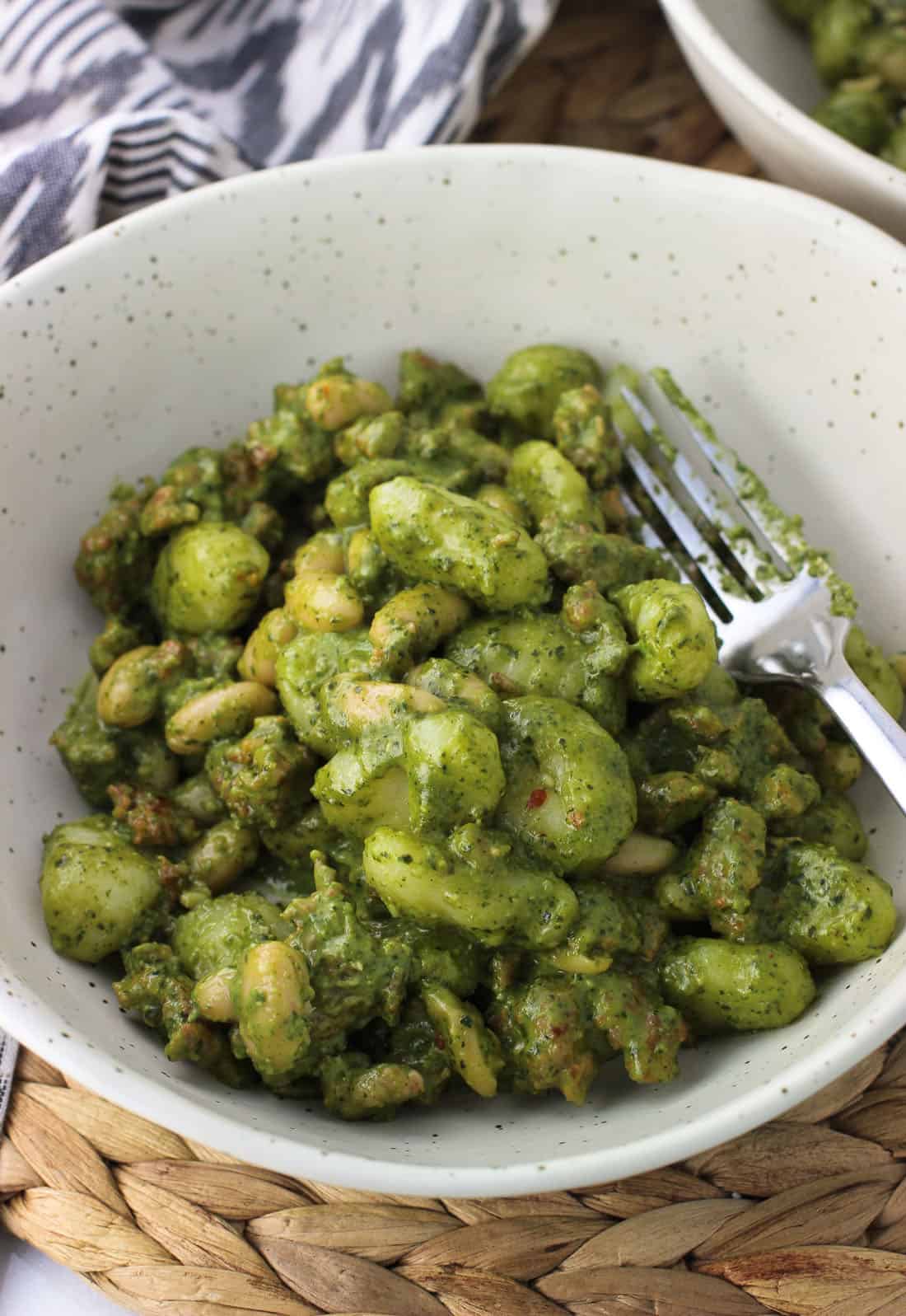 A dish of gnocchi, white beans, and sausage covered in a creamy pesto sauce with a fork.