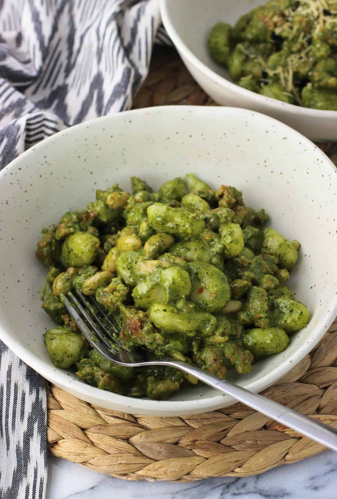 A dish filled with pesto gnocchi with a fork with another dish in the background.