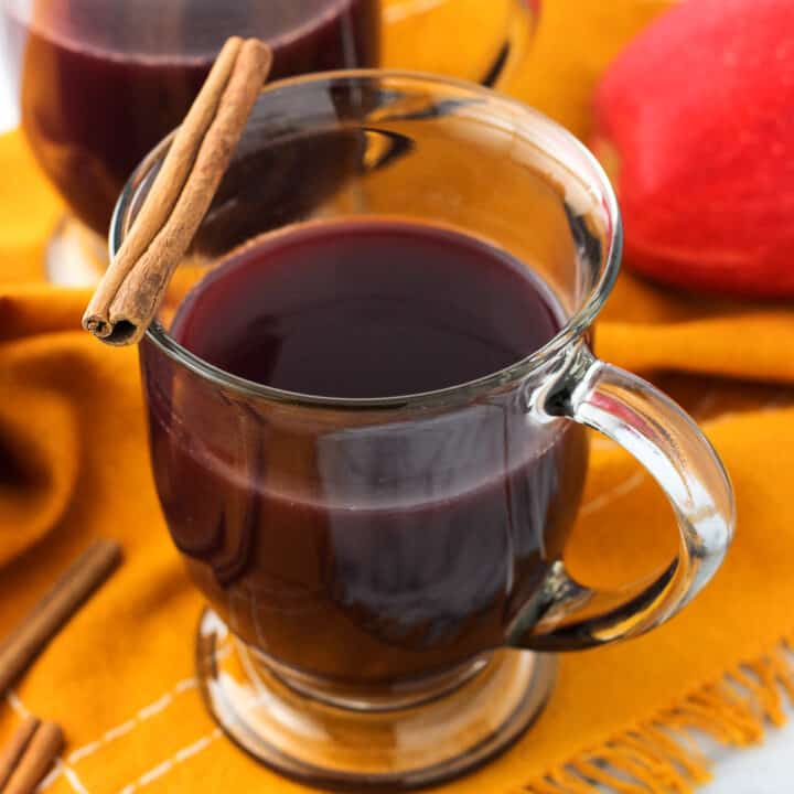 Two clear glass mugs of mulled wine garnished with cinnamon sticks