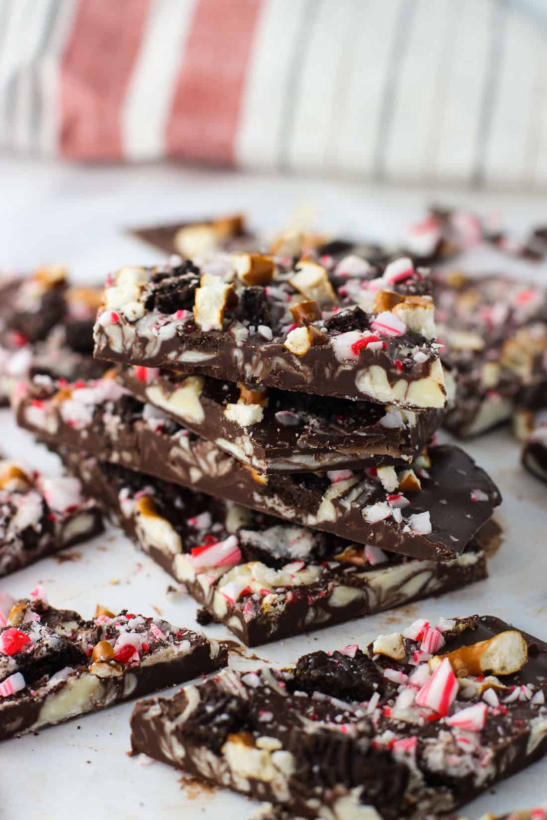 A stack of four peppermint bark pieces on a sheet of parchment, surrounded by other pieces of bark.