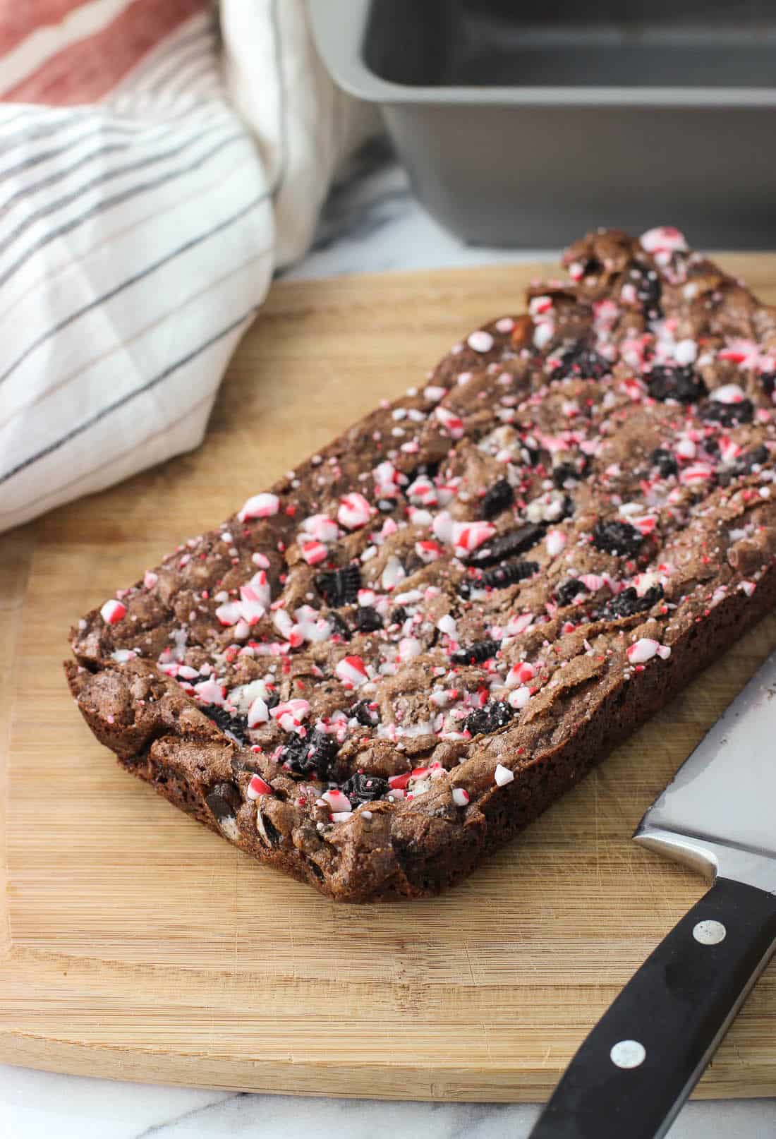 A 9" x 5" slab of brownies on a wooden cutting board before being cut into slices