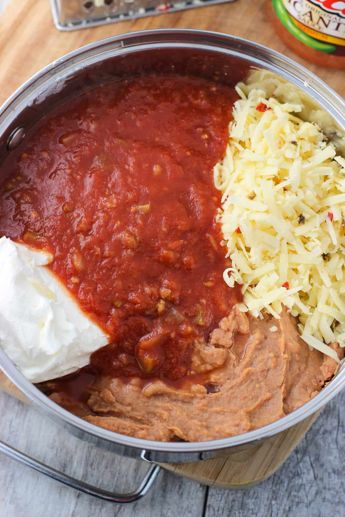 A medium saucepan filed with picante sauce, cream cheese, grated pepperjack cheese, and refried beans