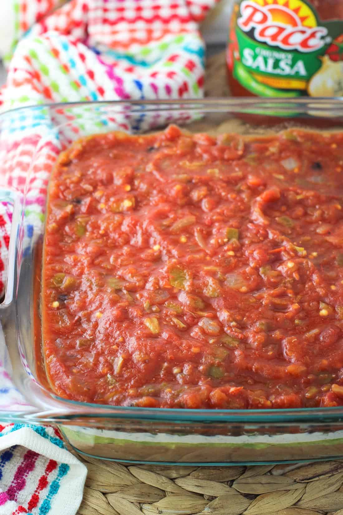 Seven layer dip in a glass baking dish, with the salsa layer on top