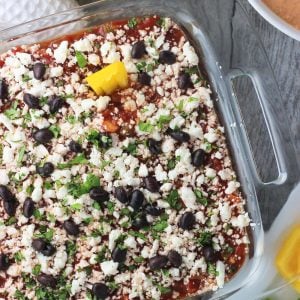 An overhead picture of seven layer dip in a clear glass 8"x8" dish next to a bowl of hot blended dip and a bowl of tortilla chips