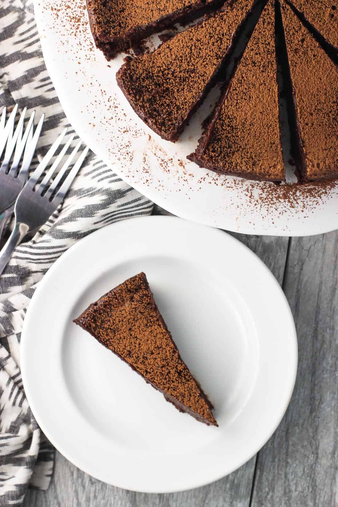 Sliced ckae on a cake stand next to a pile of forks and one slice on a dessert plate