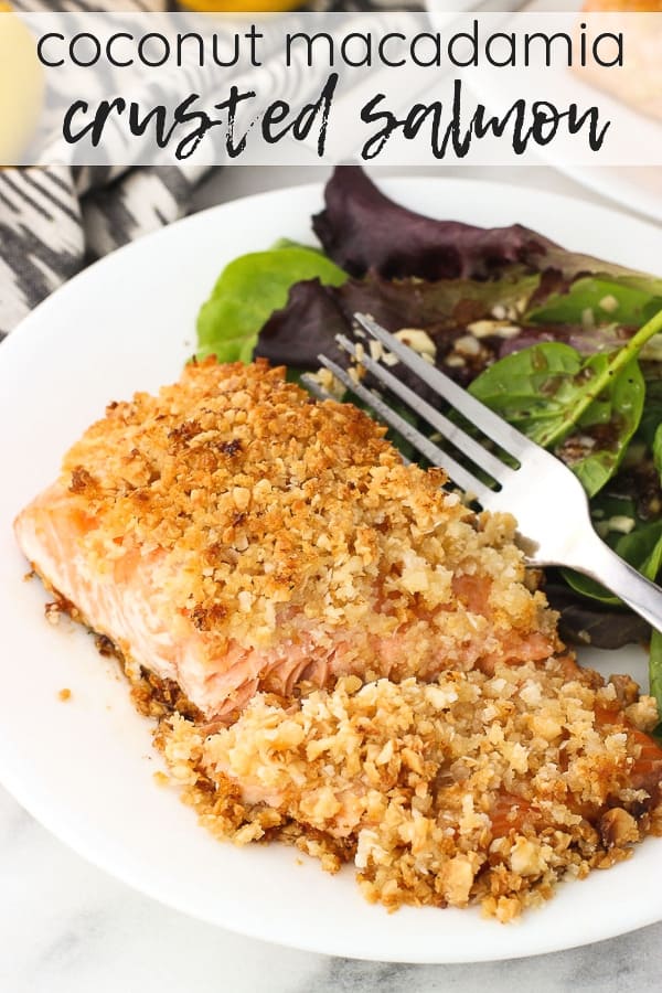 A crusted fillet of salmon cut in half on a plate with a side salad and a fork.