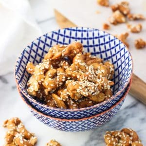 Cashew clusters topped with sesame seeds in a small ceramic bowl surrounded by more clusters