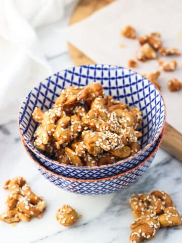 Cashew clusters topped with sesame seeds in a small ceramic bowl surrounded by more clusters