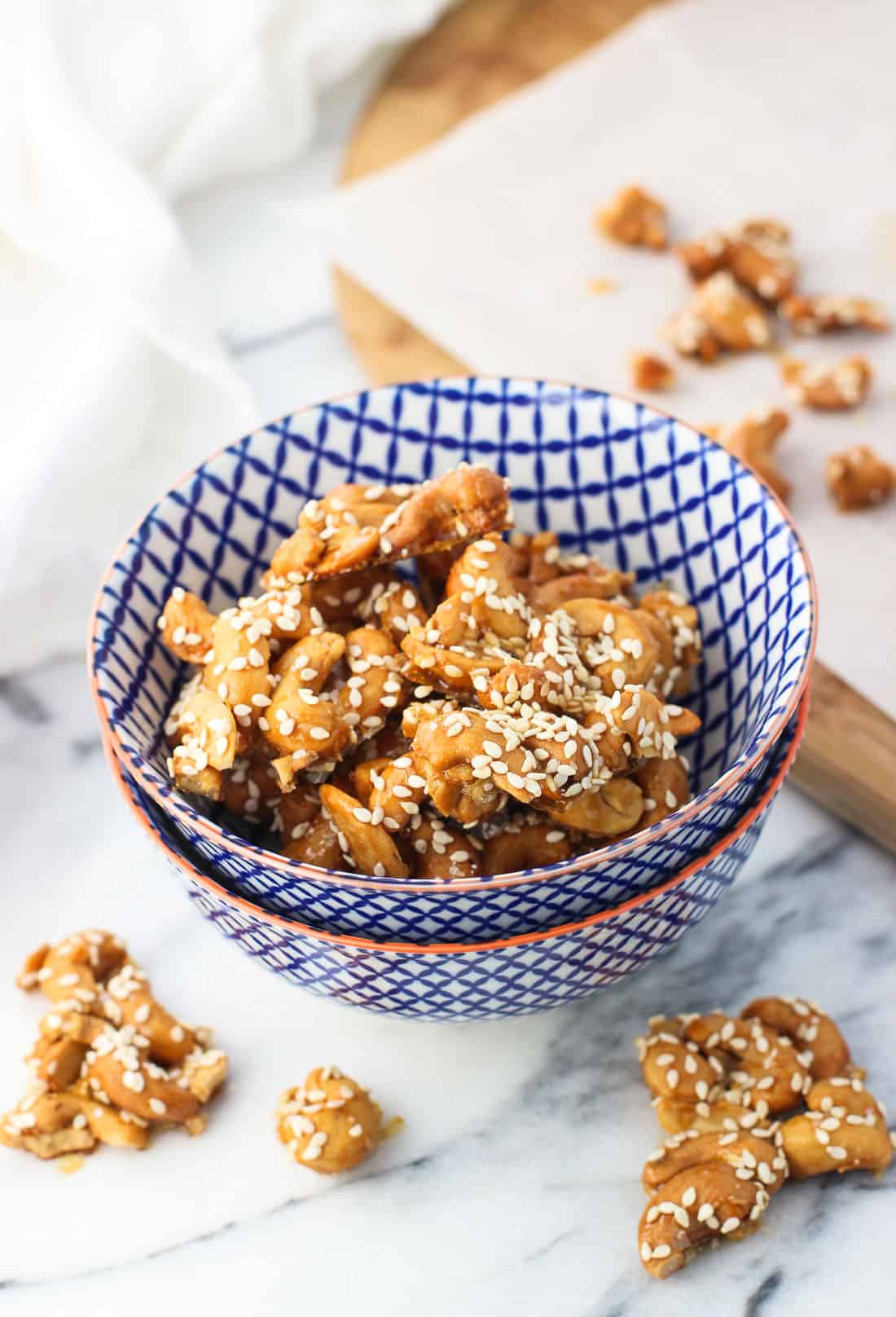 Cashew clusters topped with sesame seeds in a small ceramic bowl surrounded by more clusters