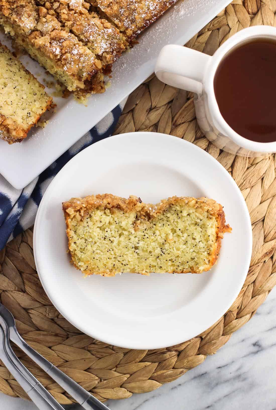 An overhead picture of a slice of bread on a small plate next to the rest of the bread loaf and a mug of tea