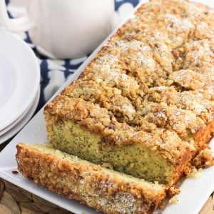 Sliced lemon poppy seed bread on a rectangular serving plate with a mug of tea in the background