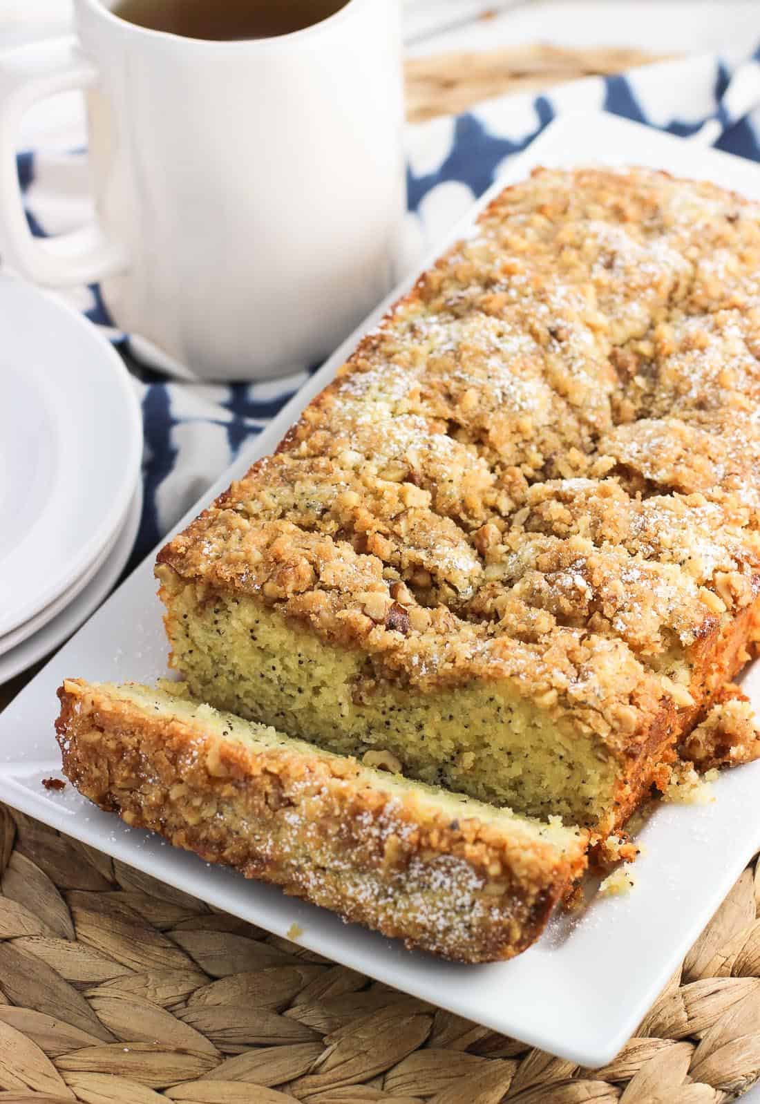 Sliced lemon poppy seed bread on a rectangular serving plate with a mug of tea in the background