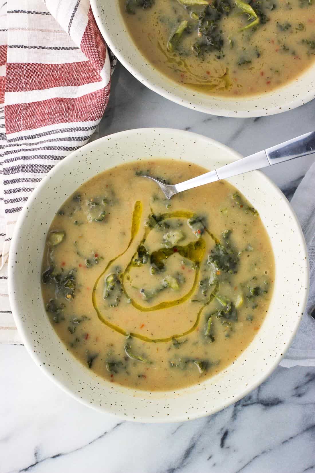 An overhead shot of two bowls of soup, one with a spoon in it and drizzled with olive oil