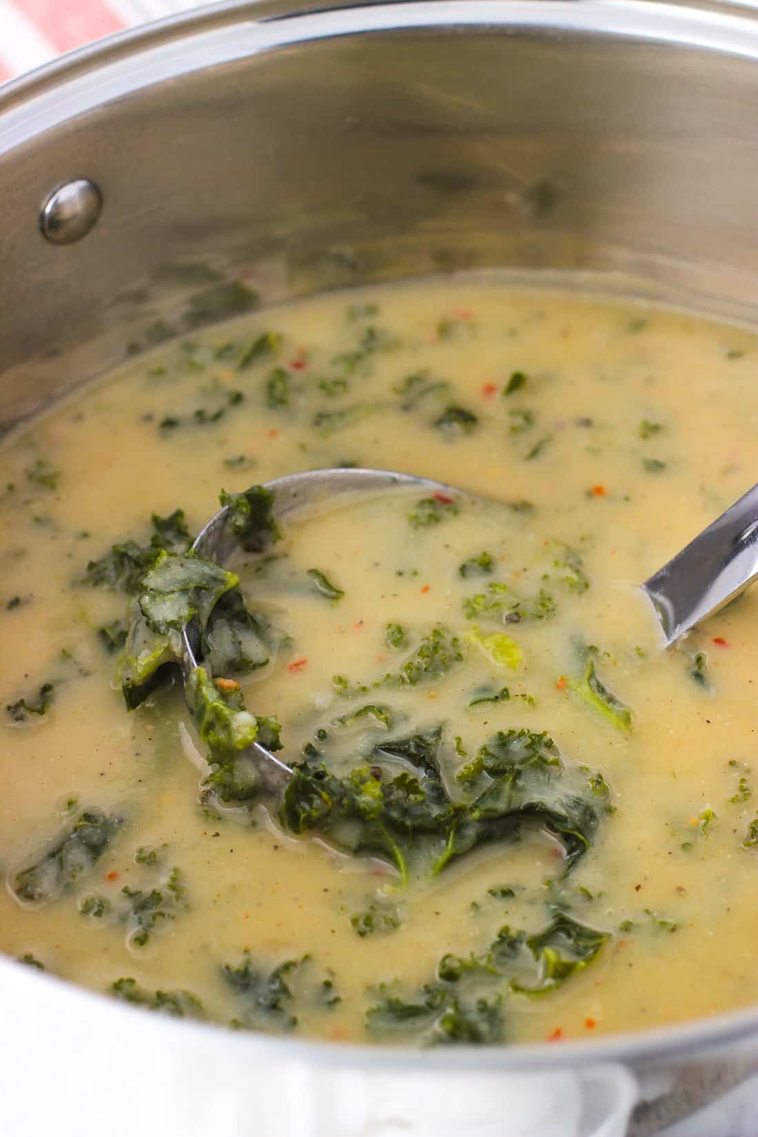 A ladle of soup featuring lots of kale being lifted out of a metal pot of soup